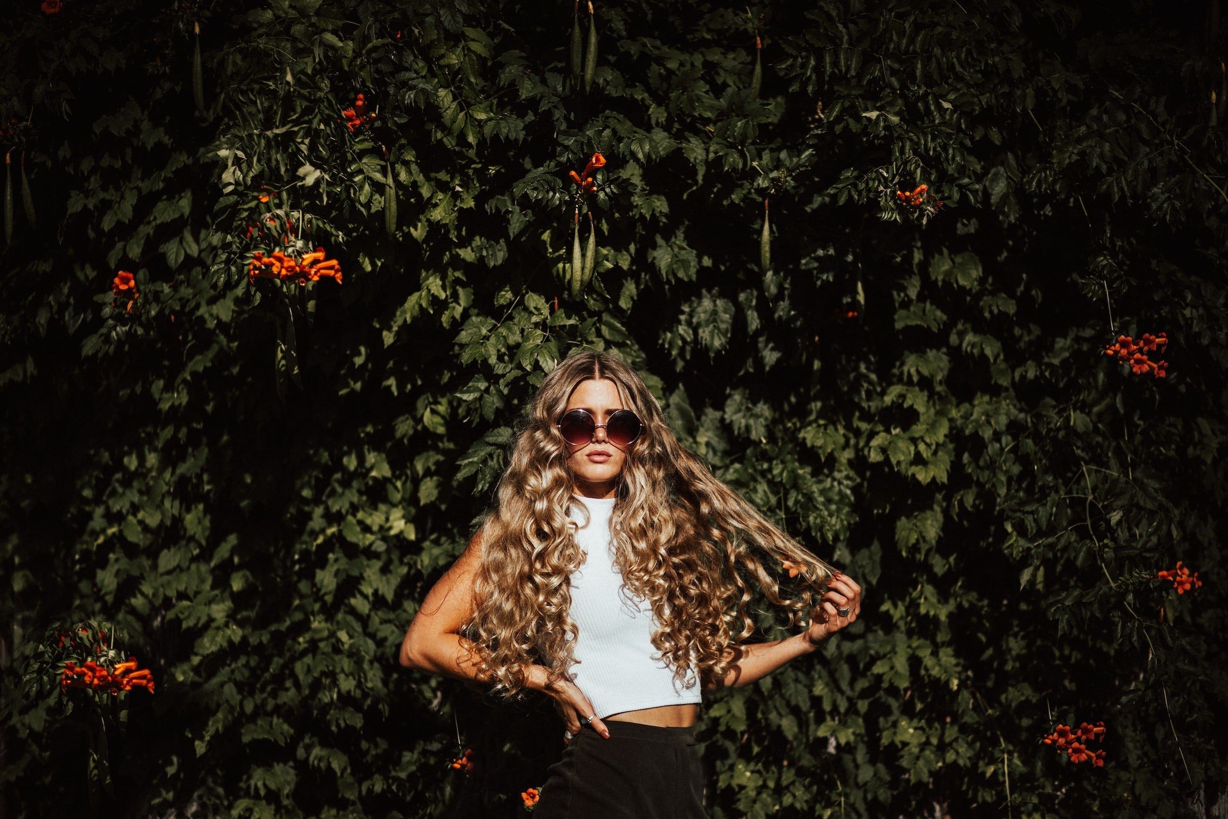 Woman with long voluminous curls in front of greenery