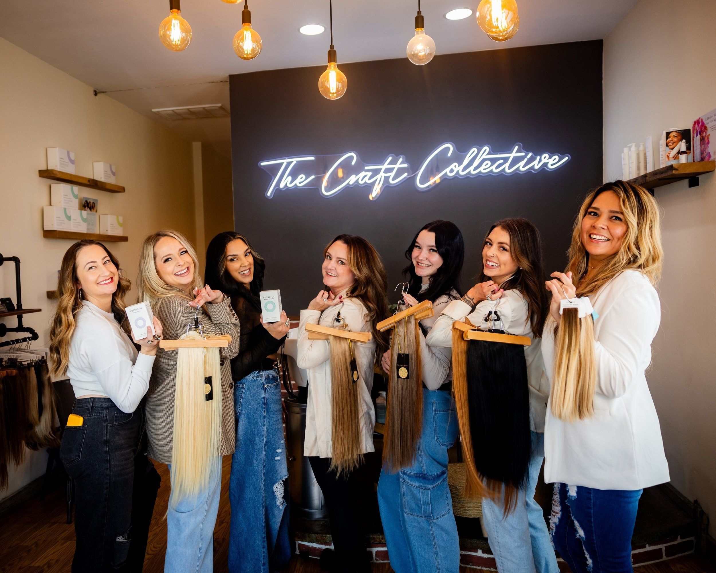 The Craft Collective team holding hair extension bundles under the salon's neon sign