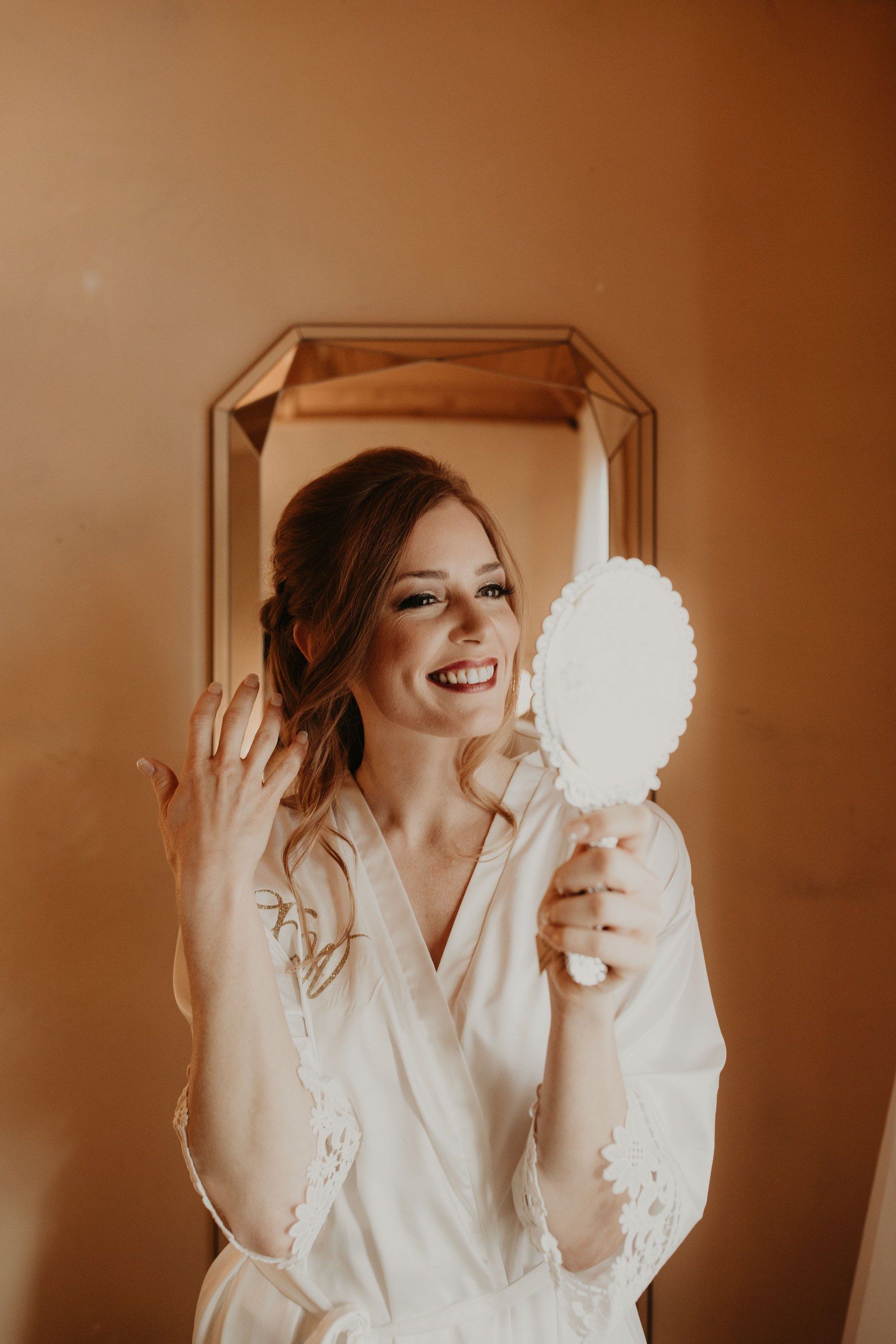 Bride smiling into a hand mirror